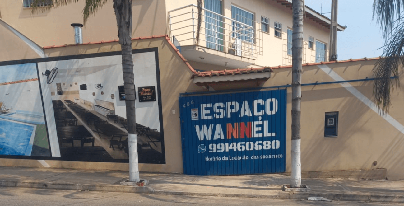 Fachada do Espaço Wannel com portão azul e área de lazer ao fundo