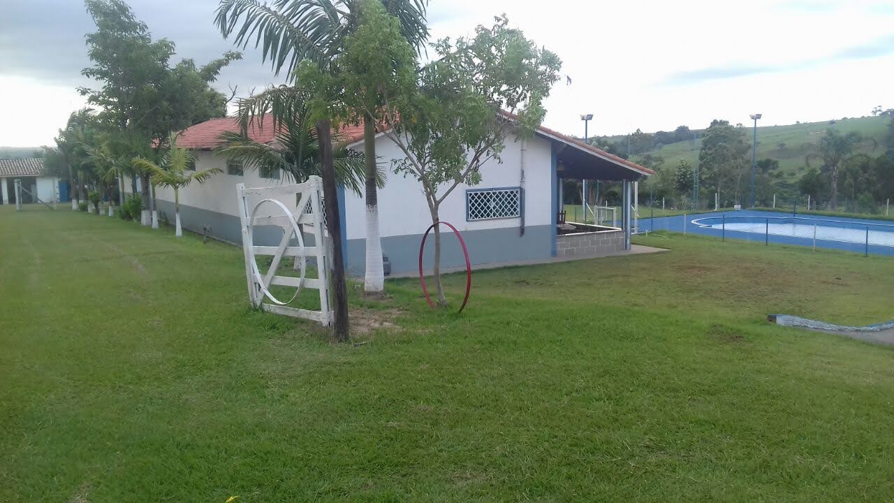 Vista diurna do Espaço Campestre Wannel com casa, piscina, gramado verde e portão branco